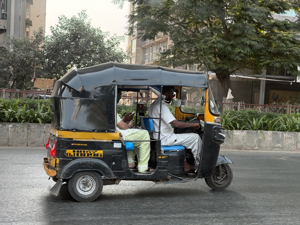 A black-and-yellow auto rickshaw crossing a Mumbai street