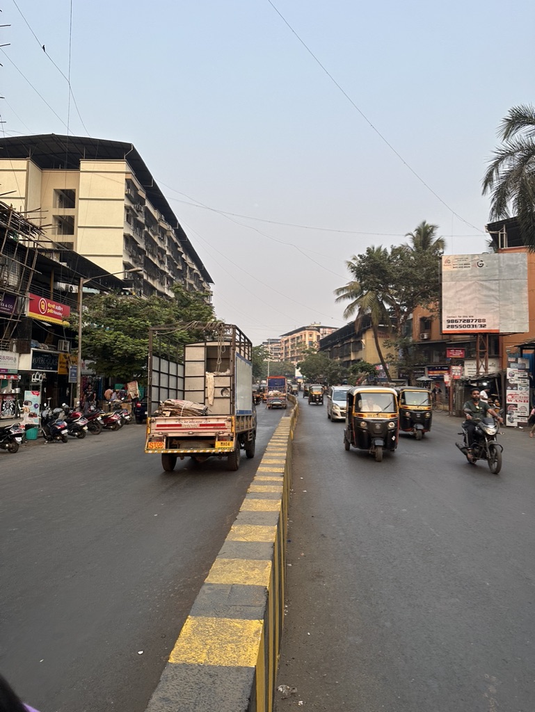 A divided suburban road, rickshaws and a motorbike sharing the lane